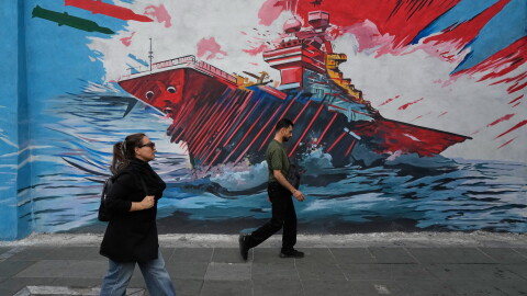 People walk past a mural depicting a U.S. aircraft carrier under missile attack by Iran in downtown Tehran, on May 17. The two countries agreed to a ceasefire but strikes have continued including U.S. military strikes against Iranian targets on Monday.