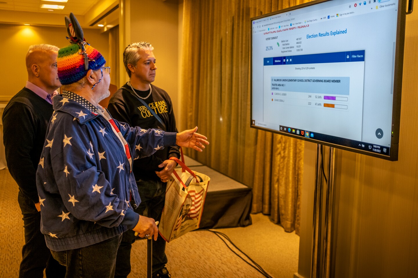 (From front to back) San Diego residents Nicole Murray-Ramirez, Bob Lehmen and Eddie Reynoso watch as results come in at the San Diego County Democratic Party election night watch party in downtown San Diego, Nov. 8, 2022.