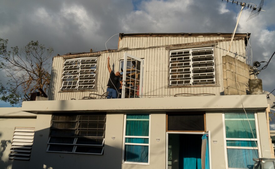 Lopez tries to move a cable by the door of his home built above his mother's cement house. He says he wasn't aware of any building codes at the time of construction. There are some 75,000 homes built without permits on the island, according to government figures.