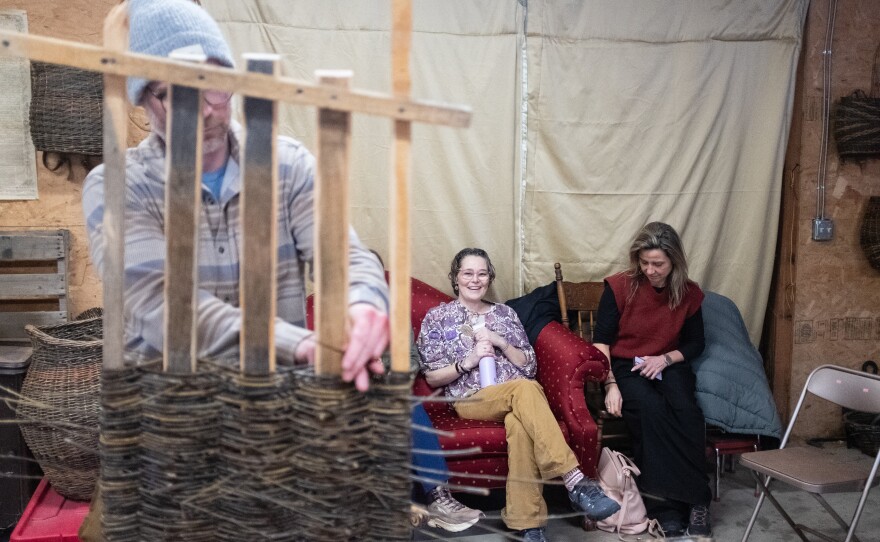 David D'Amico takes a turn weaving the back of the tray while MaddyChristine Hope Brokopp and Cynthia Siegers look on.