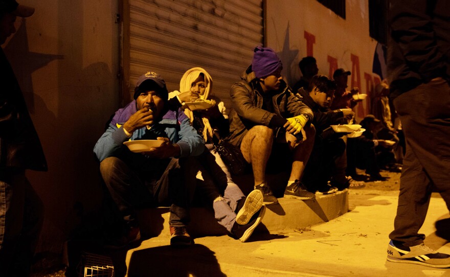 Migrants eat under the orange hue of a blinking street light. The gallons of stew are gone in a heartbeat. Even though they fed hundreds that night, Lilian Mejía can't help but tear up when she announces the food's gone to those who didn't get any. "They're so hungry, you just want to feed all of them but it's impossible," she says.