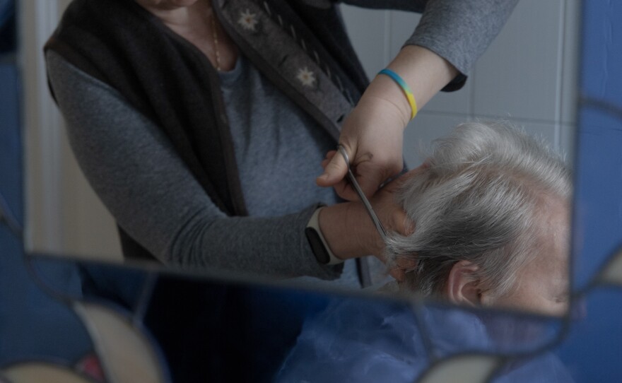 Caregiver Liliya Khodunay cuts Anna's hair in Anna's home in Milan, Italy, in February 2023.