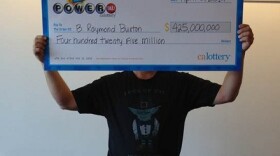 This photo provided by the California Lottery shows Powerball winner B. Raymond Buxton holding a check for $425 million on April 1, 2014, in Sacramento, Calif. Buxton was wearing a shirt that featured a picture of Yoda and read, "Luck of the Jedi I have."