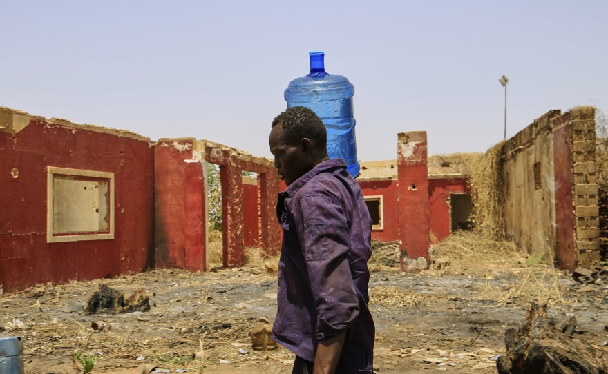 A man carries a water container past a building damaged during the civil war at a distribution point due to water outages in Khartoum, Sudan, Sunday, May 25, 2025.