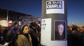 People are shown looking at drawn crosses and the portrait of the French caricaturist Georges Wolinski who was killed during a shooting at a French satirical newspaper in Paris on Jan. 7, 2015.