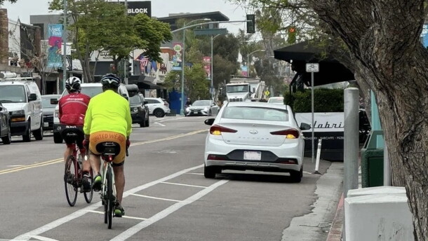 Two cyclists ride past a car parked in the bike lane of 30th Street in North Park.