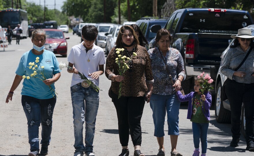 People walk with flowers to honor the victims in Tuesday's shooting at Robb Elementary School in Uvalde, Texas, Wednesday, May 25, 2022.