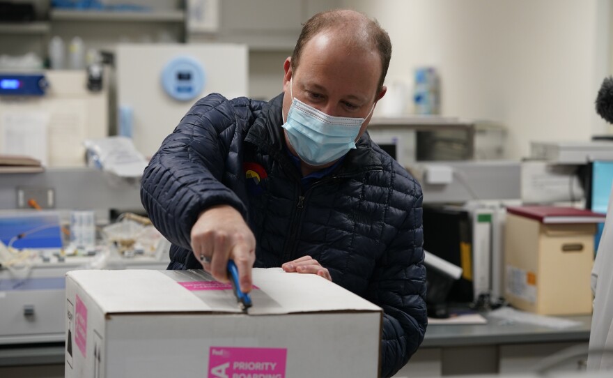 Colorado Gov. Jared Polis opens the shipping box containing the state's first shipment of COVID-19 vaccine at the Colorado Department of Public Health and Environment, Dec. 14, 2020, in east Denver.