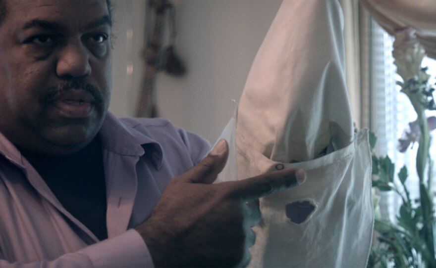 Daryl Davis displays the KKK hood from one of the many robes that have been given to him over the years by Klan member friends who have renounced their membership.