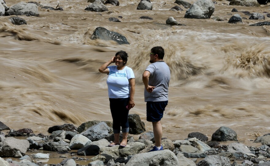 A couple looks at the overflowing Maipo River on Sunday in Santiago, where at least three people are dead and 19 others missing after heavy storms.