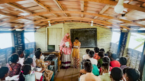 Hosne Ara teaches a group of fourth graders, seated on benches inside the floating school's classroom.