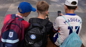FILE - Three boys use their phones while sitting outside a school in Sydney, Monday, Dec. 8, 2025.