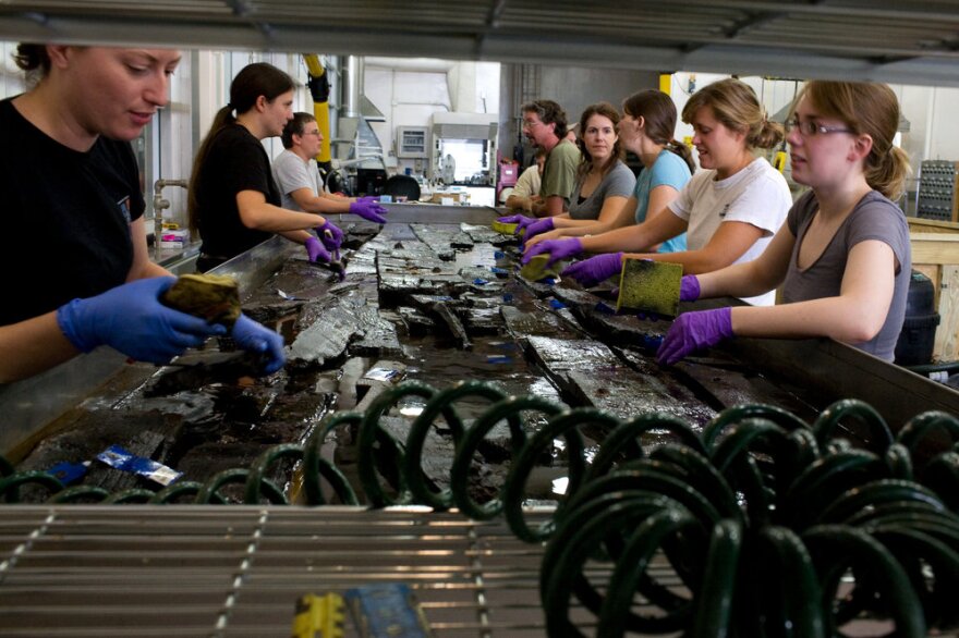 A group of conservators, curators, and volunteers at Maryland Archaeological Conservation Laboratory, drain the tank to further clean the wood planks. A heavy smell is coming out of the planks.
