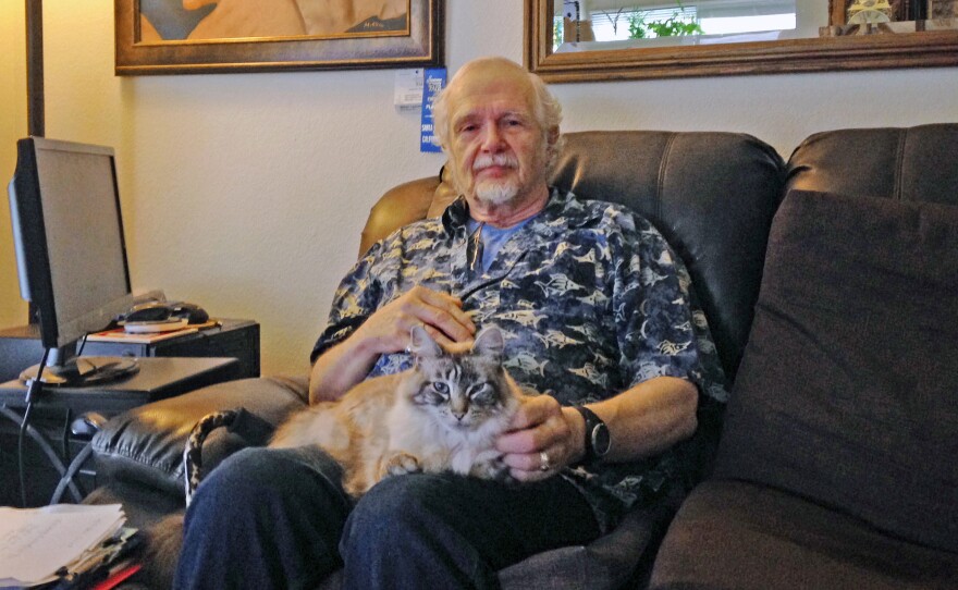 Retired California school teacher Mikkel Lawrence sits with his cat, Max. Lawrence has hepatitis C and has struggled to afford the medicine he needs to treat it.