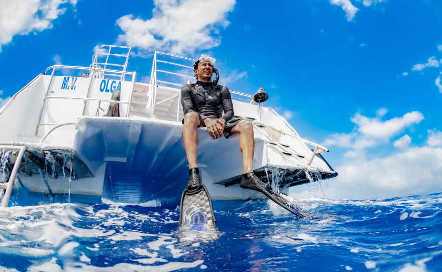 Presenter and underwater cinematographer Patrick Dykstra, fully equipped for a dive, sitting on a boat. Dominica.