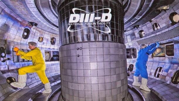 Two scientists, one wearing yellow coveralls and the other wearing blue coveralls, complete work on th DIII-D tokamak nuclear fusion reactor, operated by General Atomics in San Diego.