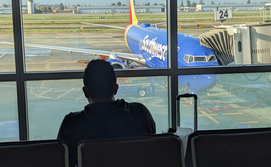 A passenger sitting inside Norman Y. Mineta San Jose International Airport with a Southwest plane in the background, Dec. 28, 2022.