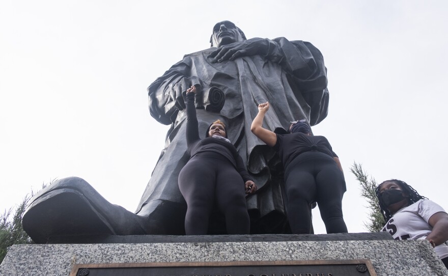 Protesters hold their fists in the air at the base of the Christopher Columbus Statue at Columbus City Hall during a protest organized against police brutality and the Columbus statue on June 27, 2020.
