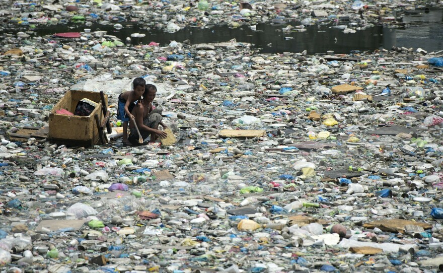 A father and son on a makeshift boat in the Philippines collect plastic bottles to sell in Manila.