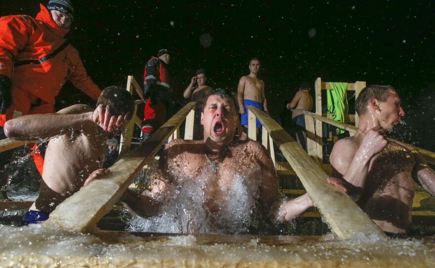 Russian Orthodox believers swim in frigid water at a pond outside St. Petersburg in the wee hours of Tuesday morning. Warmly dressed emergency medical technicians stand by in case anyone is overcome by the cold.