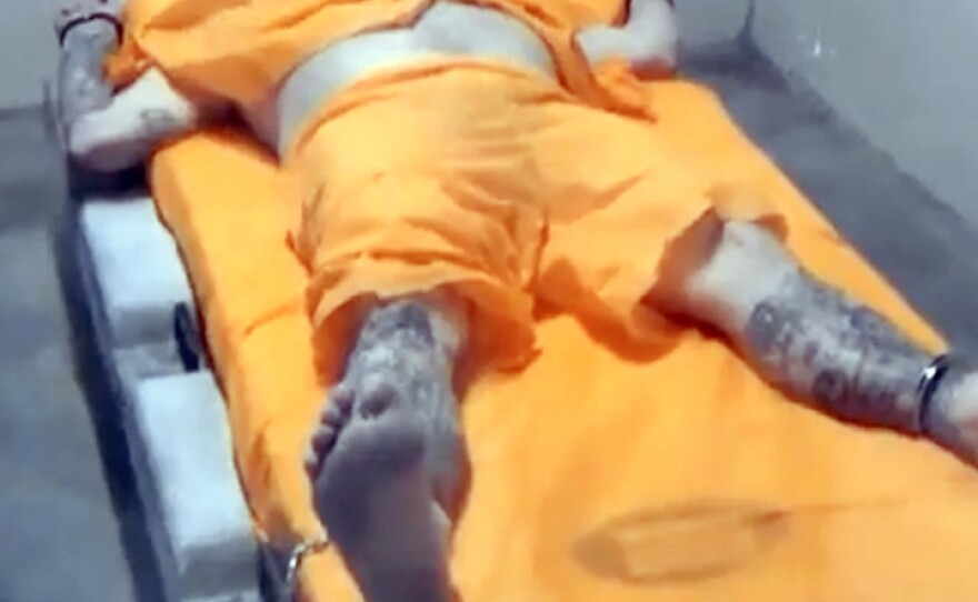 Officers at Thomson prison hold a man in a four-point restraint, with wrists and ankles secured to restrict movement.