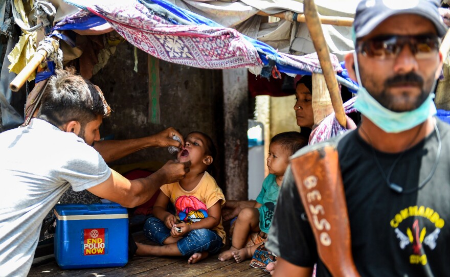 A Pakistani health worker administers the oral polio vaccine to a child during a campaign in Karachi on May 7. Because of past attacks on vaccinators, security personnel are often assigned to accompany them.