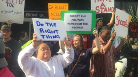 People rally and hold up signs outside of Assembly Speaker Toni Atkin's office in downtown San Diego to call for a funding increase for agencies that provide services to those with developmental disabilities, Dec. 10, 2015.