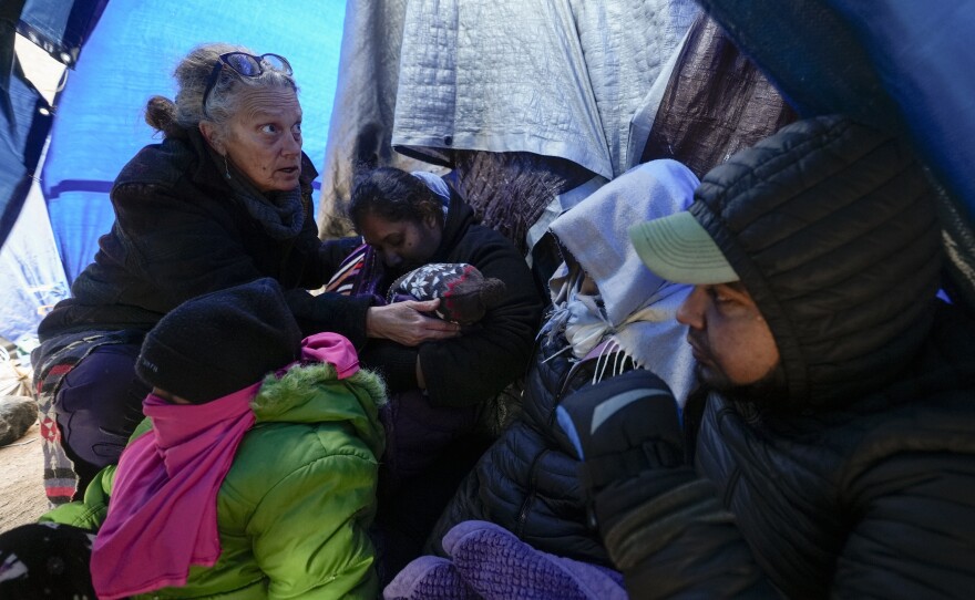 Medical volunteer Karen Parker, left, touches a 2-year-old child with a fever as she talks to a family of asylum-seeking migrants as they wait to be processed in a makeshift, mountainous campsite after crossing the border with Mexico, Feb. 2, 2024, near Jacumba Hot Springs, Calif.