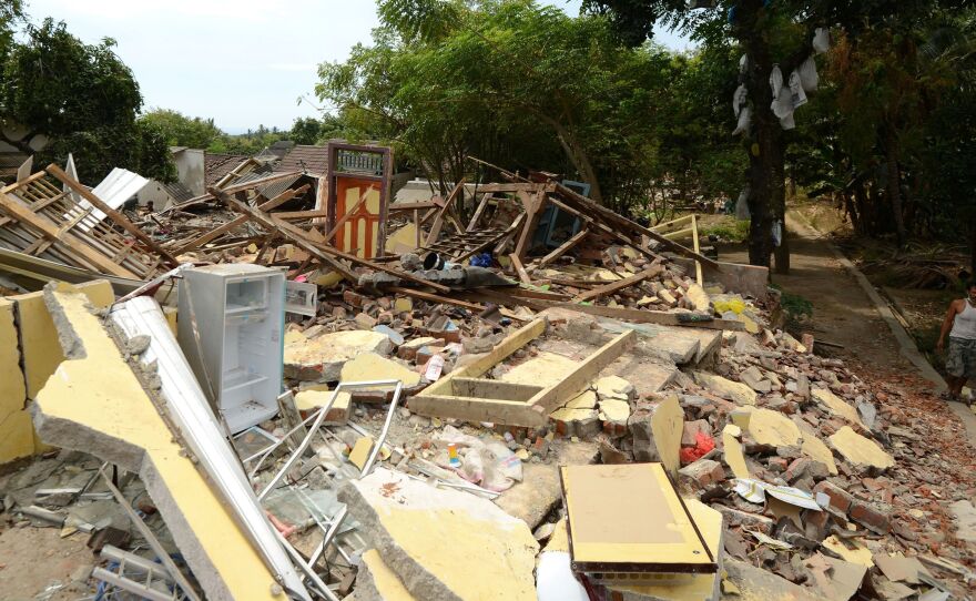 A man walks past collapsed houses in Kayangan, on the Indonesian island of Lombok, on Thursday. A devastating earthquake on Sunday killed hundreds, and a strong aftershock on Thursday caused panic among evacuees.