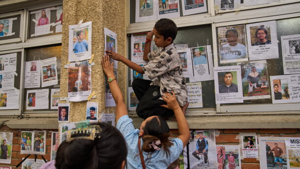 A young boy is helped by a women to put up a photograph of her missing relative on a wall alongside photographs of missing and deceased people displayed outside a government hospital in Kathmandu, Nepal, Sunday, Aug. 30, 2026.