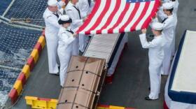 Sailors commit a casket into the sea during a burial at sea ceremony for 22 veterans and family members aboard the amphibious assault ship USS Peleliu (LHA 5).