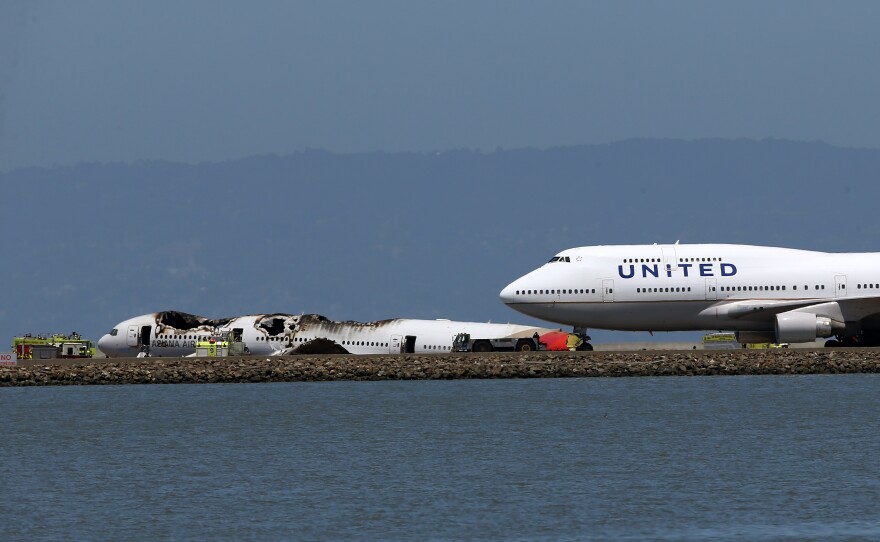 A United Airlines plane taxis on the runway with the Asiana Airlines plane in the background. After initially halting all flights, the airport slowly cleared the way for some flights.