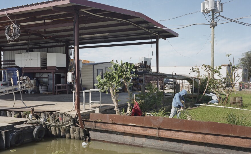Lê's <em>November 9, Graffiti, New Orleans, Louisiana</em> shows three men gardening in a small plot of land next to the water.