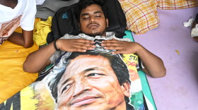 A reclining protestor covers himself with a banner printed with a portrait of Sonam Wangchuk, a prominent activist who was forcefully transferred to a hospital by the police as he staged a hunger strike in support of a movement led by Cockroach Janta Party, at a protest in New Delhi, India, Wednesday, July 22, 2026.