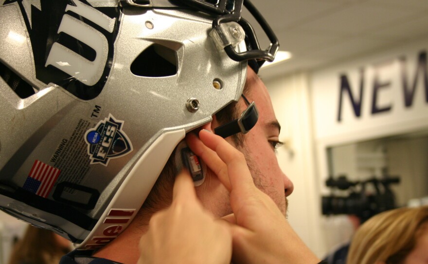 A tiny sensor is placed behind the ear of a University of New Hampshire football player. These sensors track the force and frequency of hits to the head during play.