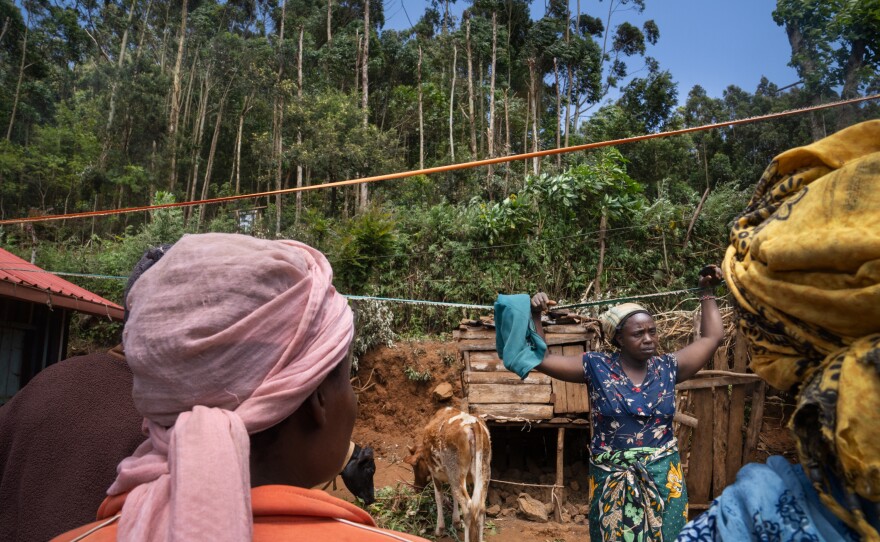 Rudia Nyuroka talks with neighbors in her yard. They all collect water from trees in the forest that towers just up the hill from their homes.