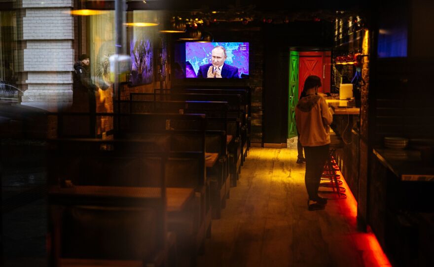 Through a restaurant window, a TV screen shows Russian President Vladimir Putin addressing his annual news conference, in Moscow on Dec. 17, 2020.