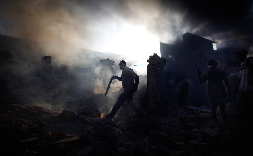 A man carries a shotgun as he walks through a collapsed burning building while trying to keep looters at bay in the commercial district of downtown Port-au-Prince.