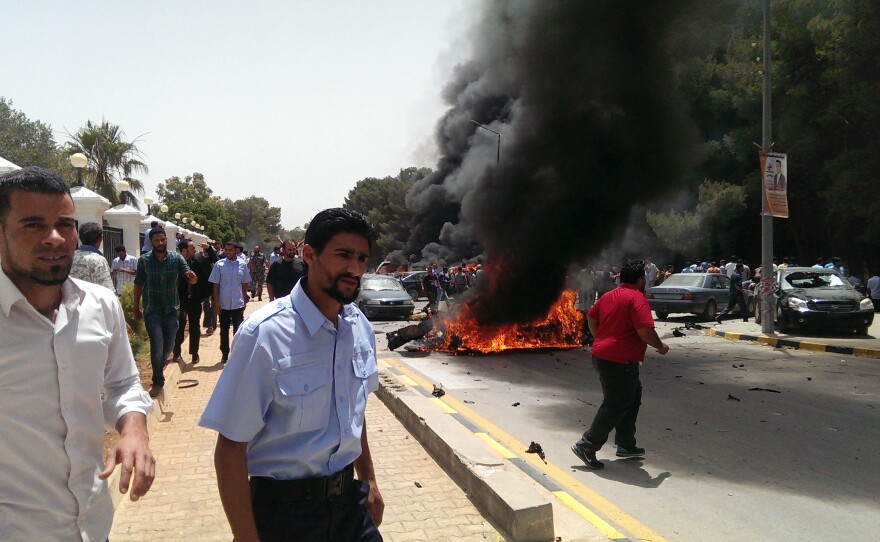 People stand near a burning car that exploded outside the parliament building, where members were drafting the new Libyan constitution, on Thursday. There were no casualties, but the blast was part of the ongoing violence in the country.