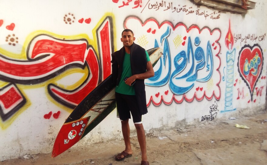 Ali Erheem, 25, poses next to graffiti on the front of his family's house in the Gaza Strip. Erheem is a member of the informal Gaza Surf Club. His painted his secondhand surfboard to look like a Palestinian flag.