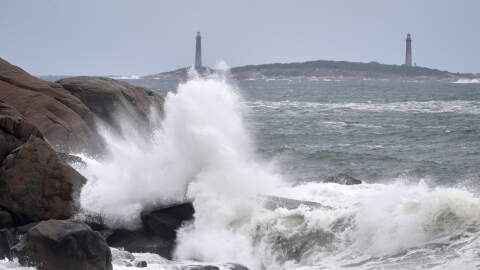 Surf breaks along the rocky coastline, with the twin lighthouses of Thatcher Island visible in the distance, during the early stages of a nor'easter Friday, Sept. 25, 2026, in Gloucester, Mass.