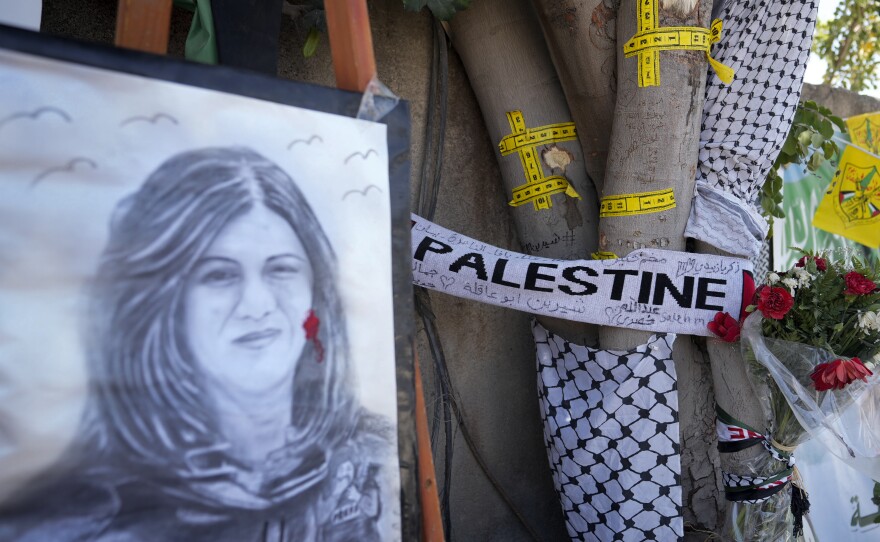 Yellow tape marks bullet holes on a tree and a portrait and flowers create a makeshift memorial on May 19, 2022, at the site where Palestinian-American Al-Jazeera journalist Shireen Abu Akleh was shot and killed in the West Bank city of Jenin.