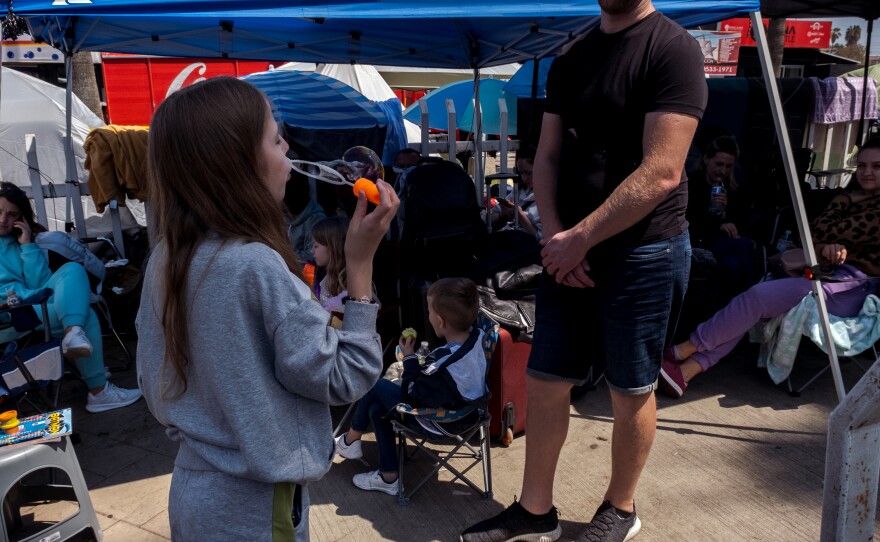 A young girl plays with her father by blowing bubbles, while she and her family wait in Tijuana for their chance to claim asylum in the United States, April 4, 2022.