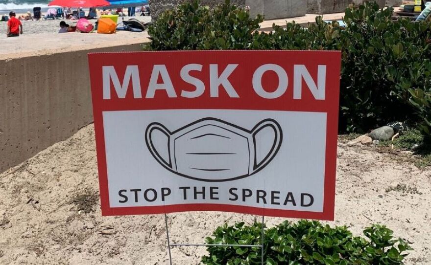 A sign in the sand encourages beachgoers to wear masks in Del Mar, July 10, 2020.