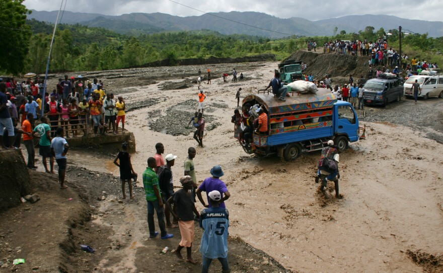 Haitians watch as people cross a river on National Route 2. Hurricane Matthew washed out a bridge at this spot cuttting off much of the southwest of the country from the capital Port au Prince.