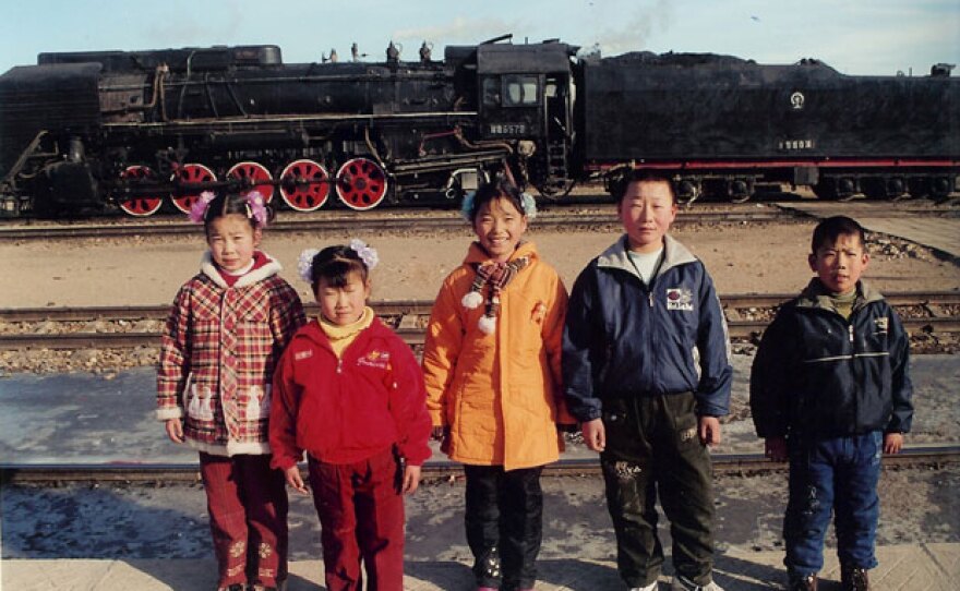 Photo of people in China standing in front of train tracks with a train in the background.