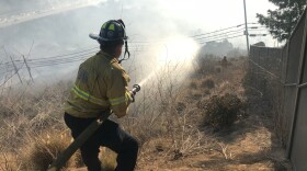 A firefighter battles a brush fire off I-8 near SDSU, June 3, 2018.