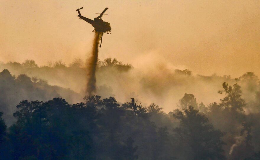 In very dense smoke from Blue Cut Fire a helicopter makes a water drop on still burning hills along Highway 2 on the way to Wrightwood.