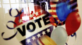 A voter is reflected in the glass frame of a poster while leaving a polling site, Nov. 1, 2016.