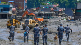 Nepalese policemen watch as earthmovers clear the debris of flash flooding in Nepal's Nuwakot district, Thursday, Aug. 27, 2026. (AP Photo/Niranjan Shrestha)